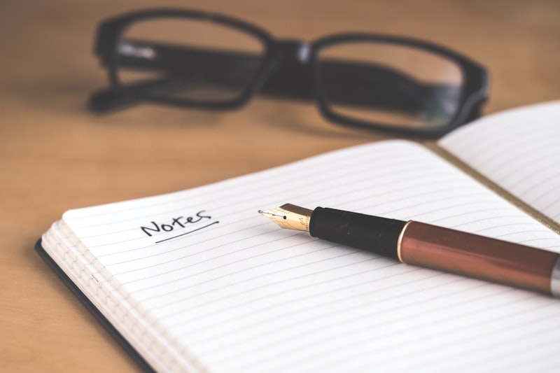 An open journal with a fountain pen and reading glasses on a warm wooden surface